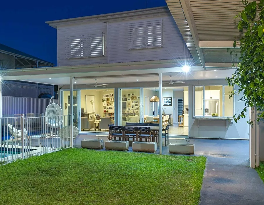 A cleaned timber deck beside a lit house and swimming pool in the evening