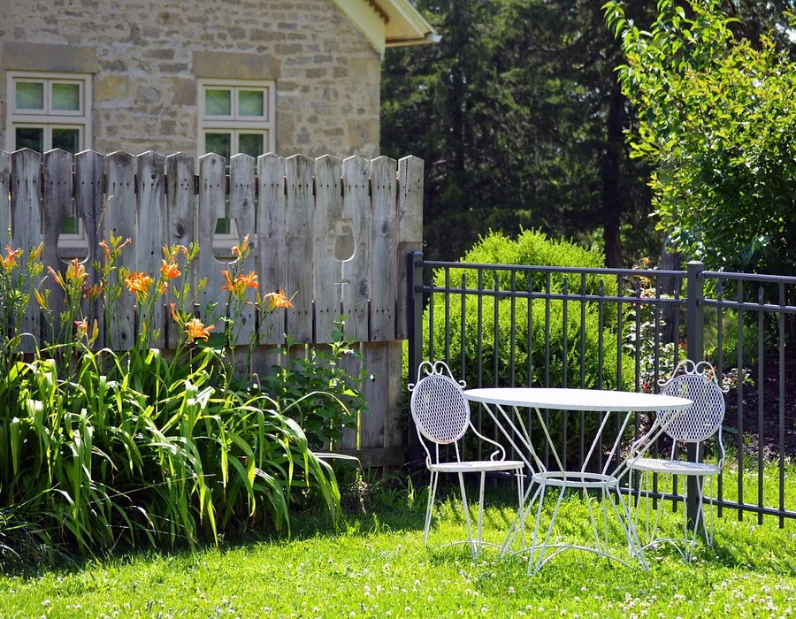 A washed picket fence behind a flower bed with garden chairs on the lawn