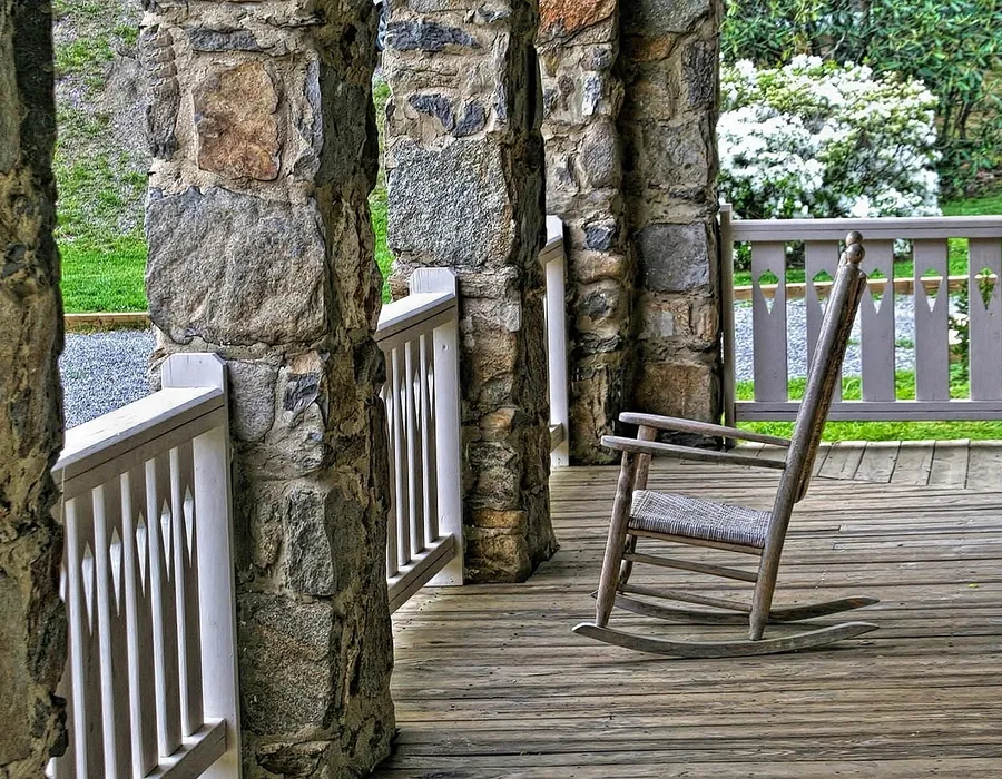 A covered porch with stone columns, a wooden rail and a rocking chair